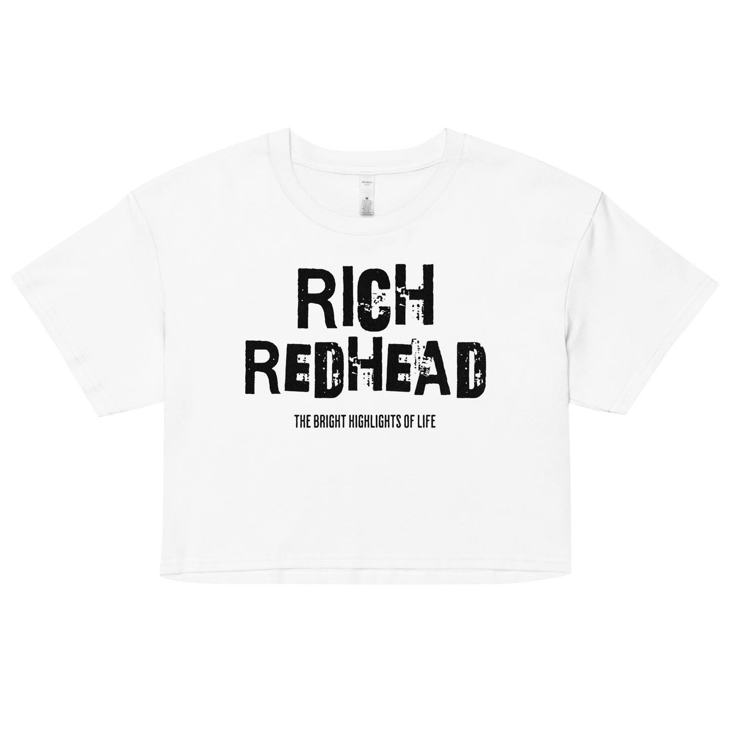 A white women’s crop top with a relaxed fit, short sleeves, and a wide crew neckline. The front features bold black distressed lettering reading “RICH REDHEAD” with the tagline “THE BRIGHT HIGHLIGHTS OF LIFE” in smaller text below.