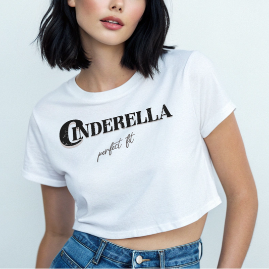 woman with jet black hair wears a White women’s crop top featuring black merger text that reads “Cinderella” with a decorative crescent moon incorporated into the letter C, and the phrase “perfect fit” written underneath in an elegant cursive script.