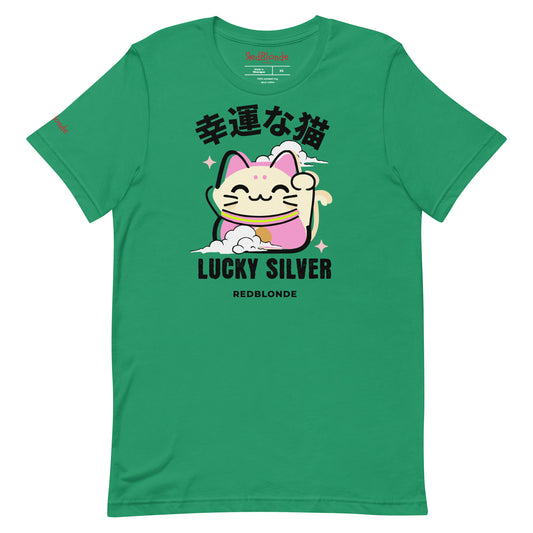A kelly green unisex T-shirt featuring a colourful illustration of a lucky cat (Maneki-neko) with pink ears and accents, smiling and waving one paw. Above the cat are Japanese characters reading "幸運な猫" (Lucky Cat), and below it are the words "LUCKY SILVER" in bold black font, followed by "REDBLONDE" in smaller text. The design is playful and cute, with stars and a cloud adding charm. The RedBlonde brand name appears in red on the inside label and on the right sleeve.