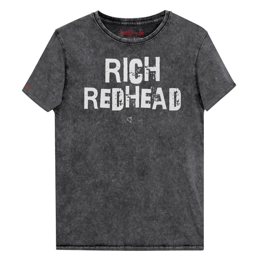 a black acid-wash unisex denim T-shirt with a distressed vintage look. The shirt features the bold white text “RICH REDHEAD” in a weathered Ed Gein font, and features the RedBlonde signature logo. The shirt has short sleeves, a crew neckline, and visible seam detailing for a rugged, casual style. Branded Redblonde on inside neck and right sleeve