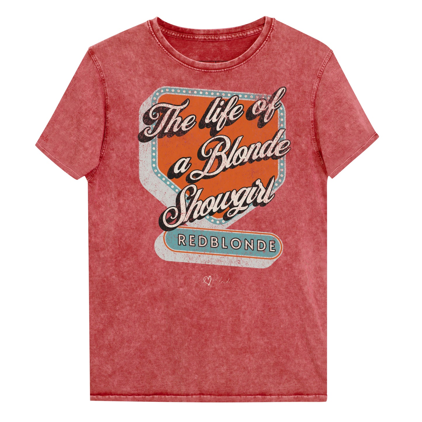 Vintage garnet red acid-wash unisex t-shirt with bold retro-style graphic text reading 'The life of a Blonde Showgirl' in white script over an orange and turquoise marquee design. The word 'RedBlonde' is displayed in turquoise block letters at the bottom, with subtle worn details giving the shirt a distressed, retro look." Branded redblonde on inside collar and right sleeve