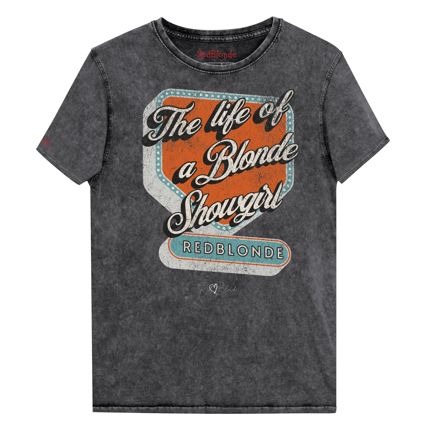 Vintage black acid-wash unisex t-shirt with bold retro-style graphic text reading 'The life of a Blonde Showgirl' in white script over an orange and turquoise marquee design. The word 'RedBlonde' is displayed in turquoise block letters at the bottom, with subtle worn details giving the shirt a distressed, retro look." Branded redblonde on inside collar and right sleeve