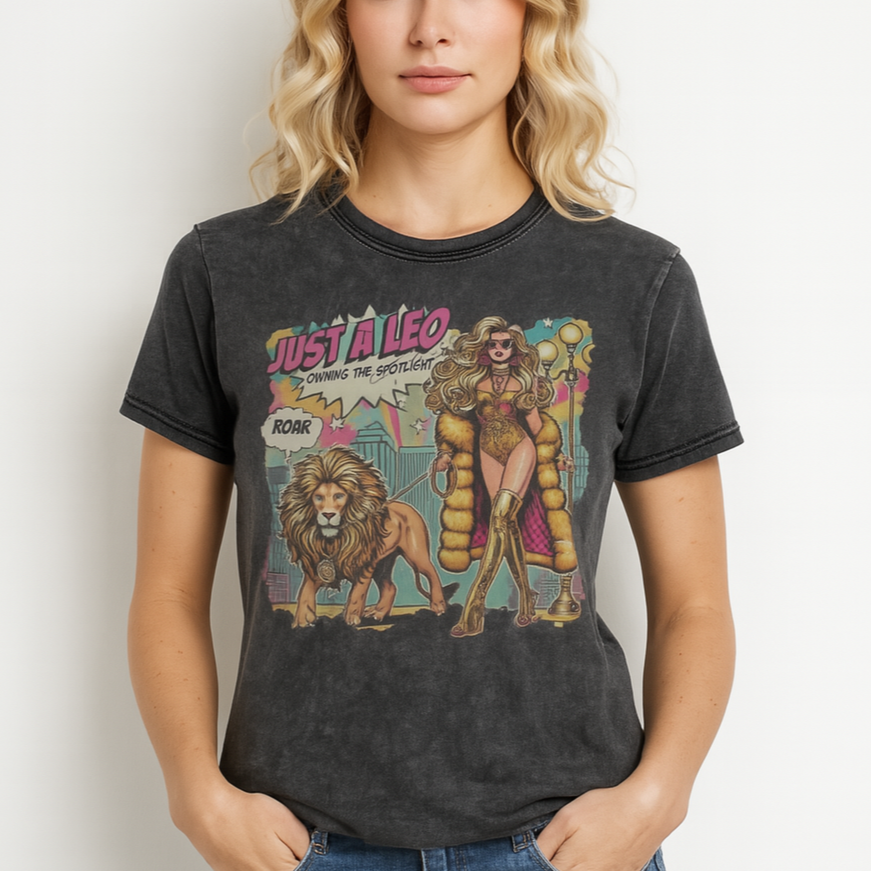 Blonde wears a unisex black denim wash vintage t-shirt with a retro pop-art Leo graphic featuring a long curly haired blonde woman in a gold swimsuit, gold over the knee boots, gold medallion and long fur coat, walking a lion on a leash wearing a gold medallion, with a caption bubble 'Roar', with a city and round bulb street lights in the background captioned ‘Just a Leo, Owning the Spotlight'. Branded RedBlonde on inside neck and right shoulder