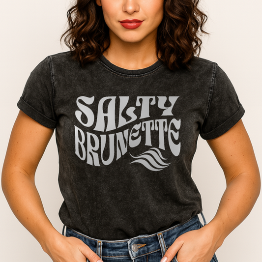 Brunette wears a soft black denim wash vintage  graphic t-shirt with the slogan 'Salty Brunette' in white retro 70s font. Branded RedBlonde in inside neck and right sleeve