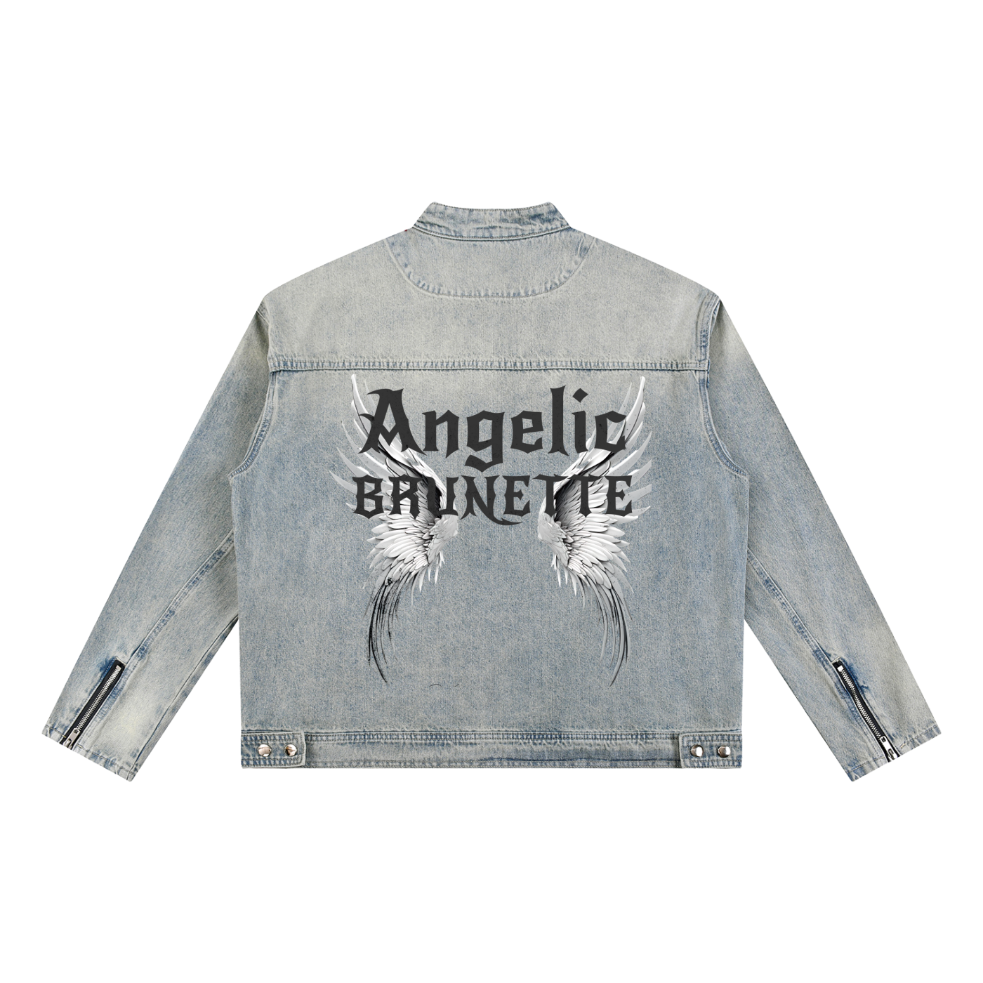 A light-wash denim jacket shown from the back on a white background. The sleeves have zippered cuffs, and the back features a large graphic with white angel wings and black gothic New Rocker style text reading “Angelic BRUNETTE.”