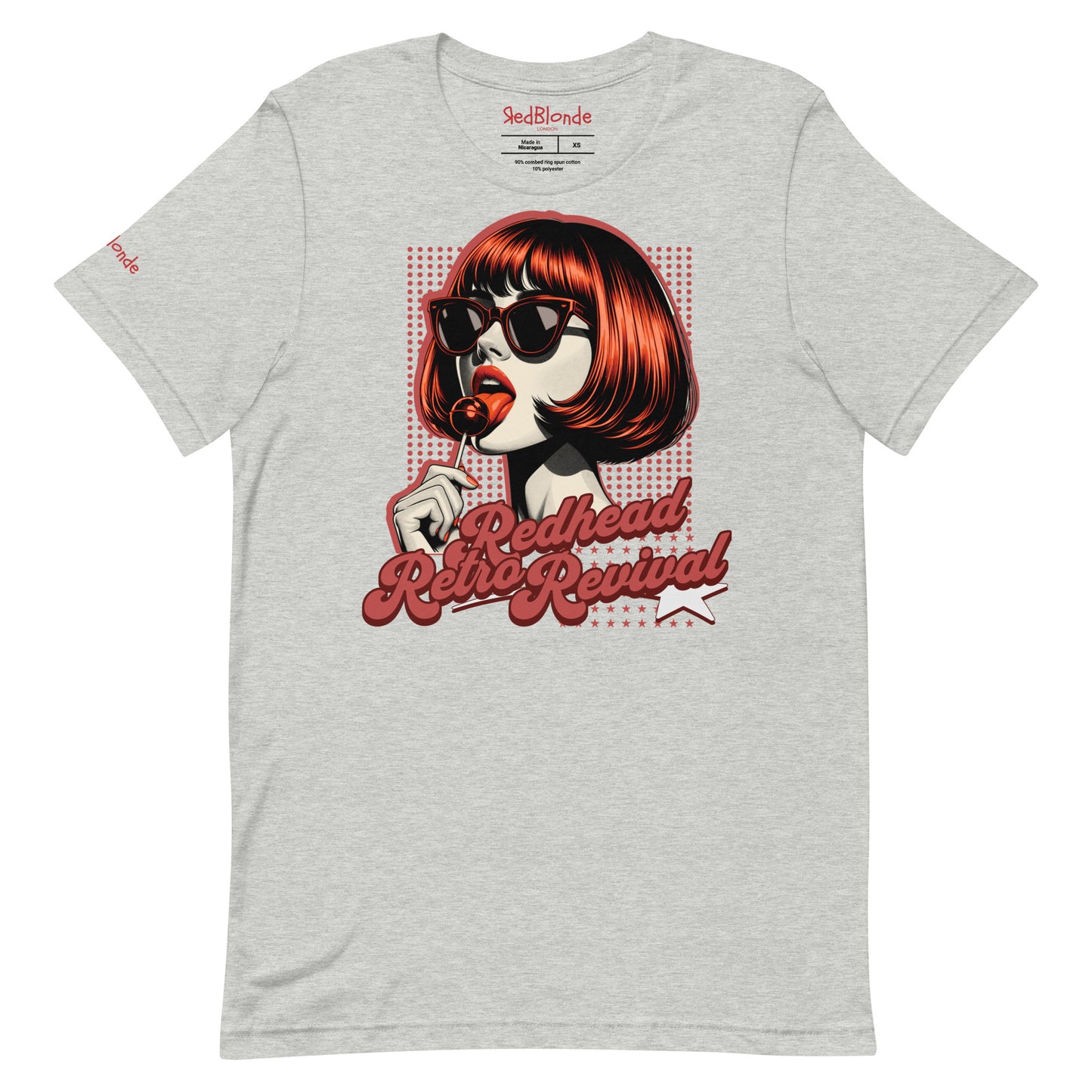 Grey unisex t-shirt featuring a bold pop-art graphic of a stylish redheaded woman with a sleek bob haircut, red lips, and black sunglasses, holding a lollipop. The design includes red halftone dots and the retro-styled slogan "Redhead Retro Revival" in cursive typography with a star accent. RedBlonde branding appears on the inner neck label and red sleeve in red text.