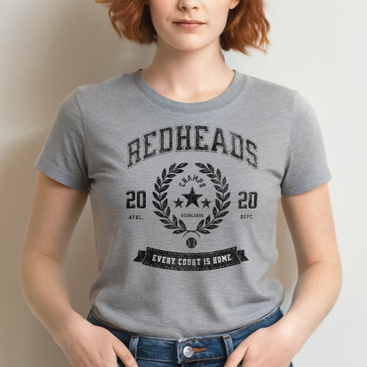 Grey unisex t-shirt with american college themed graphic featuring 'REDHEADS' in Tricot font with a laurel wreath and the words ' Champs RedBlonde' 2020 and 'every court is home' underneath. Branded RedBlonde in red on inside neck and right sleeve 