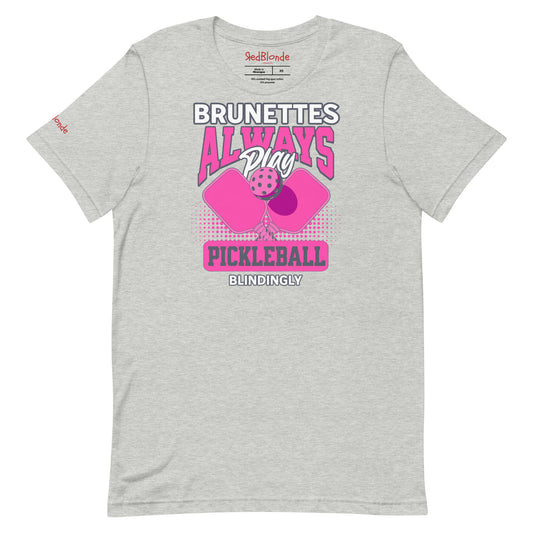 Grey unisex t-shirt with bold pink and white graphic that says "Brunettes Always Play Pickleball Blindingly," featuring two pink pickleball paddles and a ball. Branded RedBlonde on inside neck and right sleeve