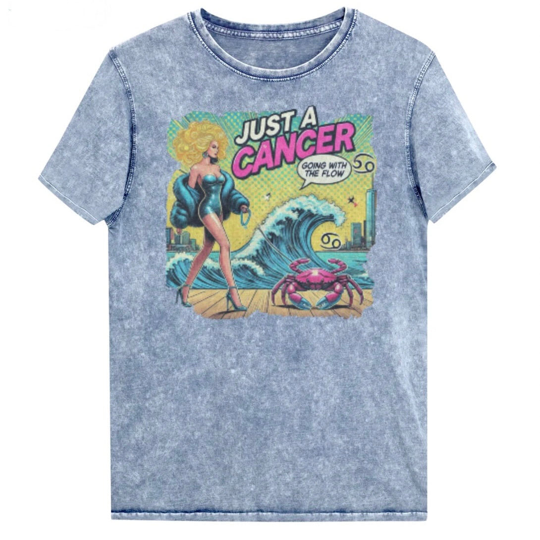 Flatlay of a unisex blue denim wash vintage t-shirt with a retro pop-art Cancer graphic featuring a blonde woman, wearing a turquoise short strapless catsuit, fur coat and strappy heels, walking a pink crab on a leash, with a high water wave and city backdrop captioned Just an Caner, Going with the Flow'. Branded RedBlonde in red on inside neck and right sleeve 