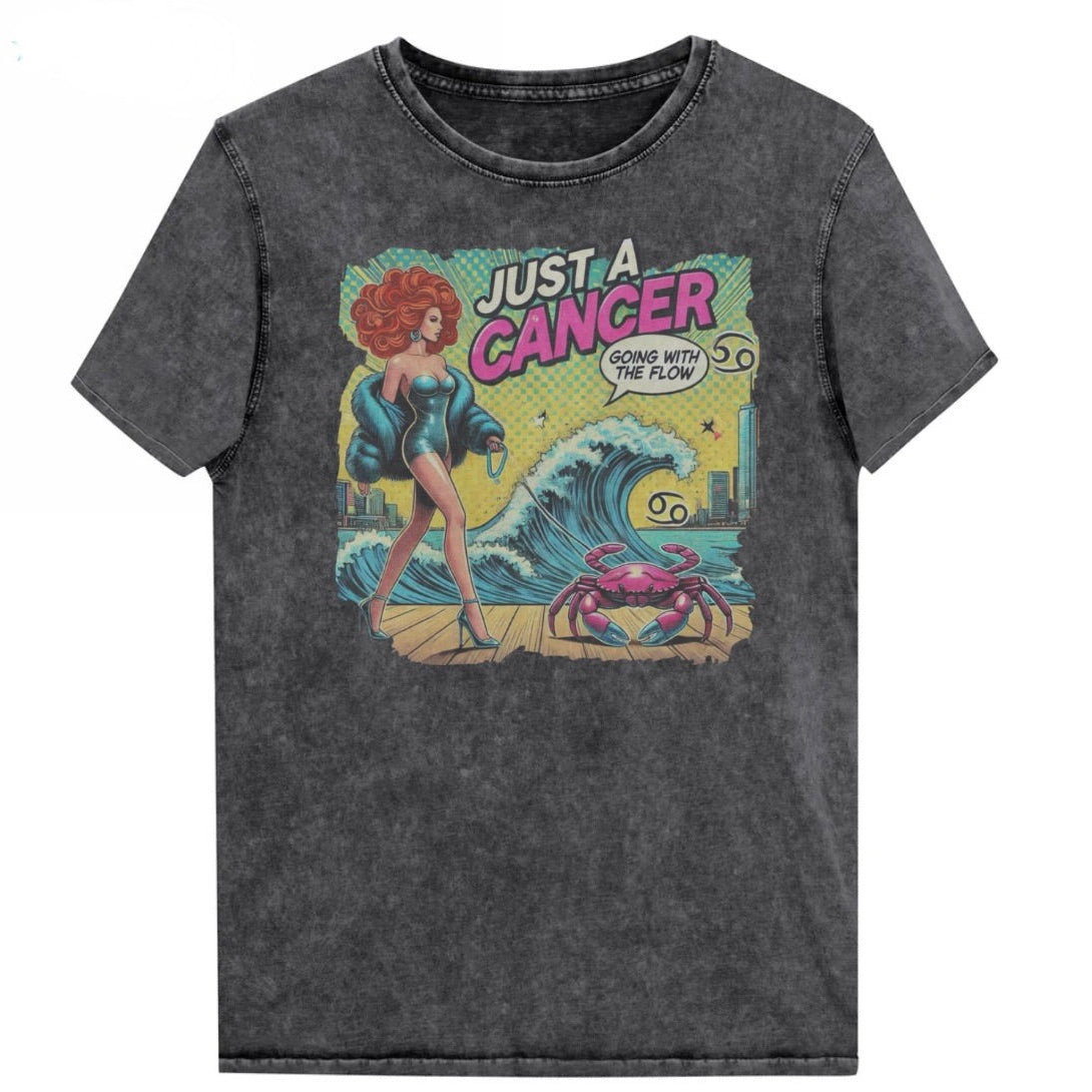 Flatlay of a unisex black denim wash vintage t-shirt with a retro pop-art Cancer graphic featuring a redhead woman, wearing a turquoise short strapless catsuit, fur coat and strappy heels, walking a pink crab on a leash, with a high water wave and city backdrop captioned Just an Caner, Going with the Flow'. Branded RedBlonde in red on inside neck and right sleeve 