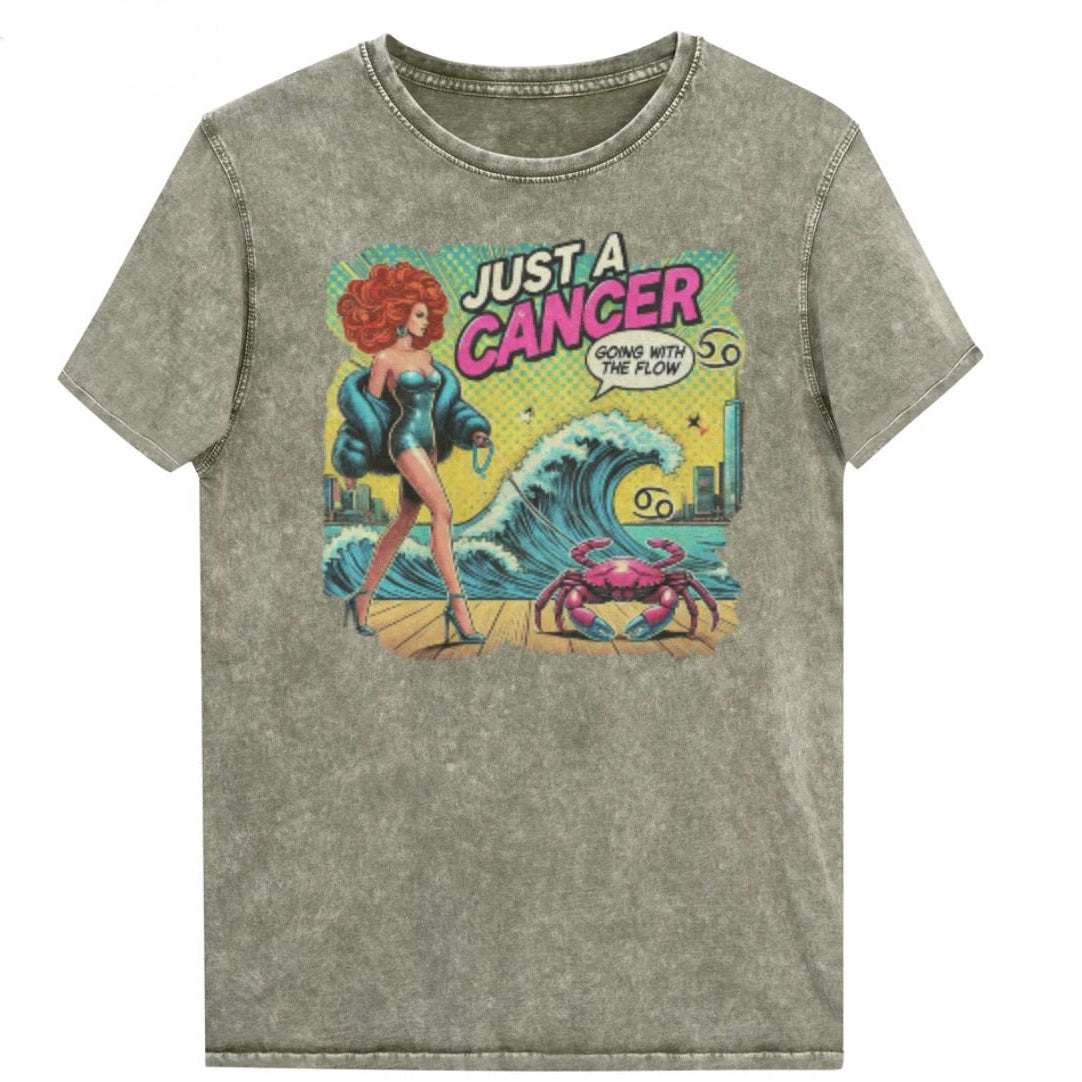 Flatlay of a unisex army green denim wash vintage t-shirt with a retro pop-art Cancer graphic featuring a redhead woman, wearing a turquoise short strapless catsuit, fur coat and strappy heels, walking a pink crab on a leash, with a high water wave and city backdrop captioned Just a Cancer, Going with the Flow'. Branded RedBlonde in red on inside neck and right sleeve 