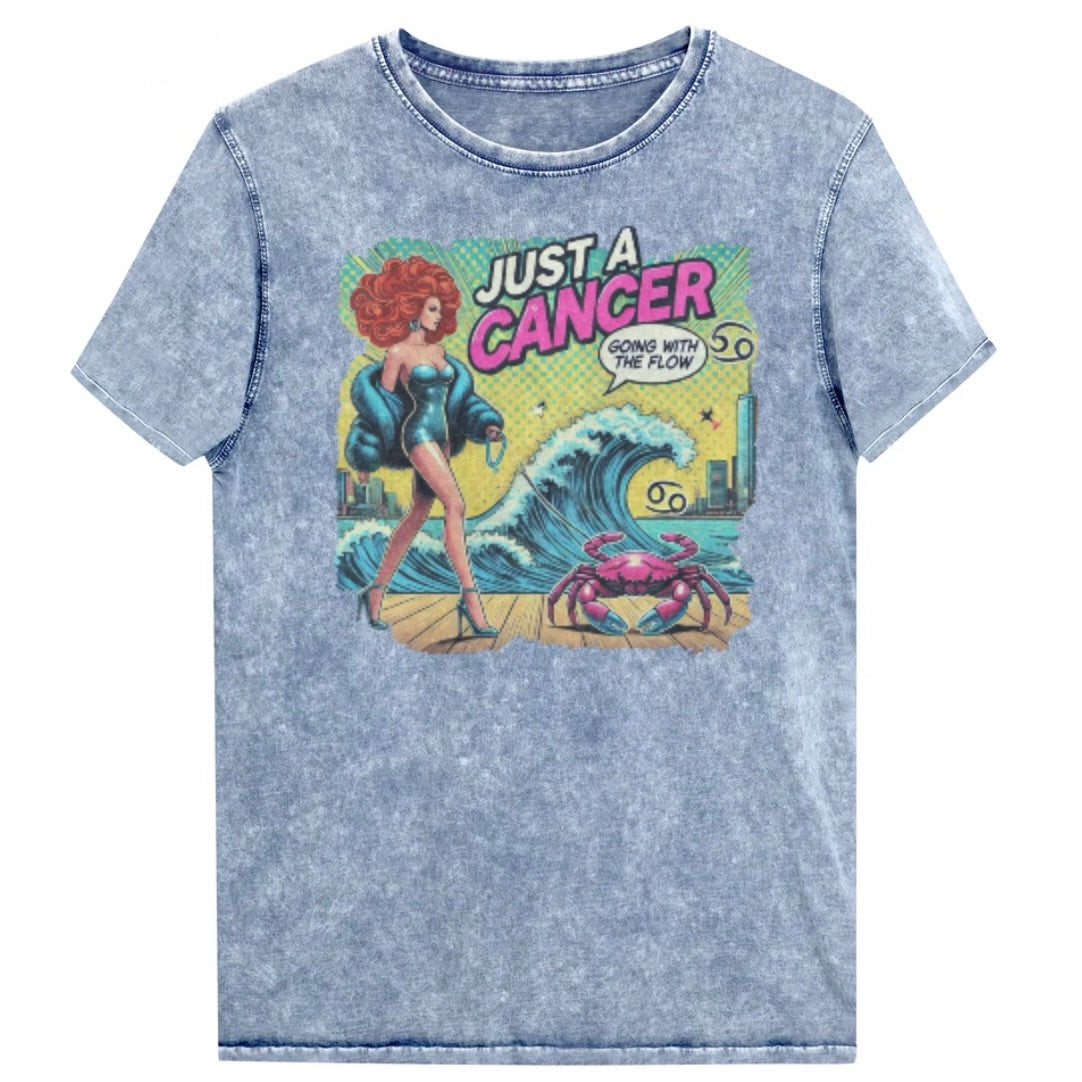 Flatlay of a unisex blue denim wash vintage t-shirt with a retro pop-art Cancer graphic featuring a redhead woman, wearing a turquoise short strapless catsuit, fur coat and strappy heels, walking a pink crab on a leash, with a high water wave and city backdrop captioned Just a Cancer, Going with the Flow'. Branded RedBlonde in red on inside neck and right sleeve 