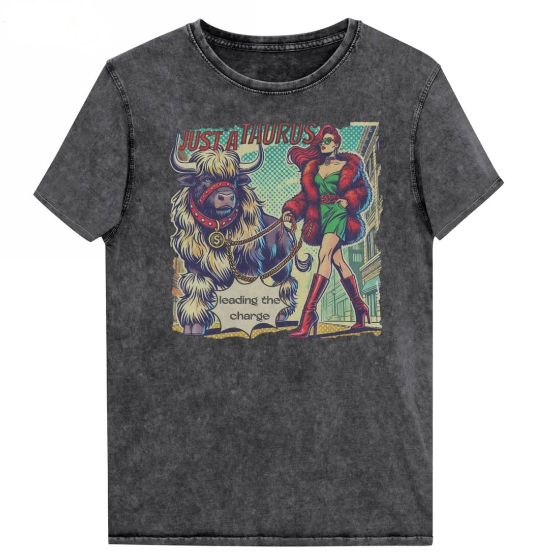 Flatlay of a unisex relaxed fit black vintage denim wash t-shirt with a retro pop-art taurus graphic featuring a redhead woman with long flowing straight hair, wearing a green dress with a red belt, red high-heeled boots and red fur coat, walking a furry bull with a red collar and medallion in city street captioned ‘Just a taurus leading the charge'. Branded RedBlonde on inside neck and right shoulder