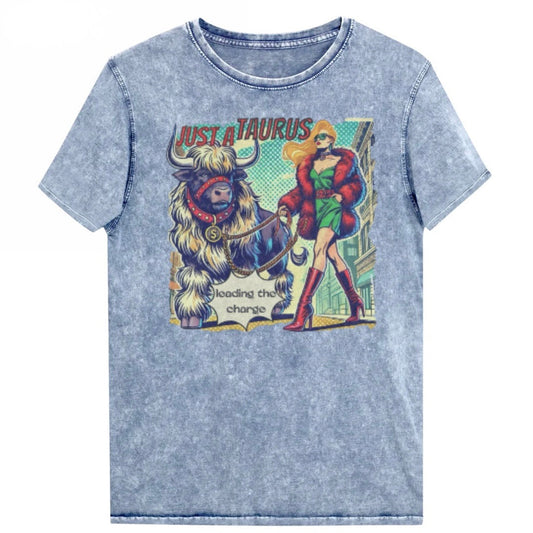 Flatlay of a unisex relaxed fit blue vintage denim wash t-shirt with a retro pop-art taurus graphic featuring a blonde woman with long flowing straight hair, wearing a green dress with a red belt, red high-heeled boots and red fur coat, walking a furry bull with a red collar and medallion in city street captioned ‘Just a taurus leading the charge'. Branded RedBlonde in red on inside neck and right shoulder