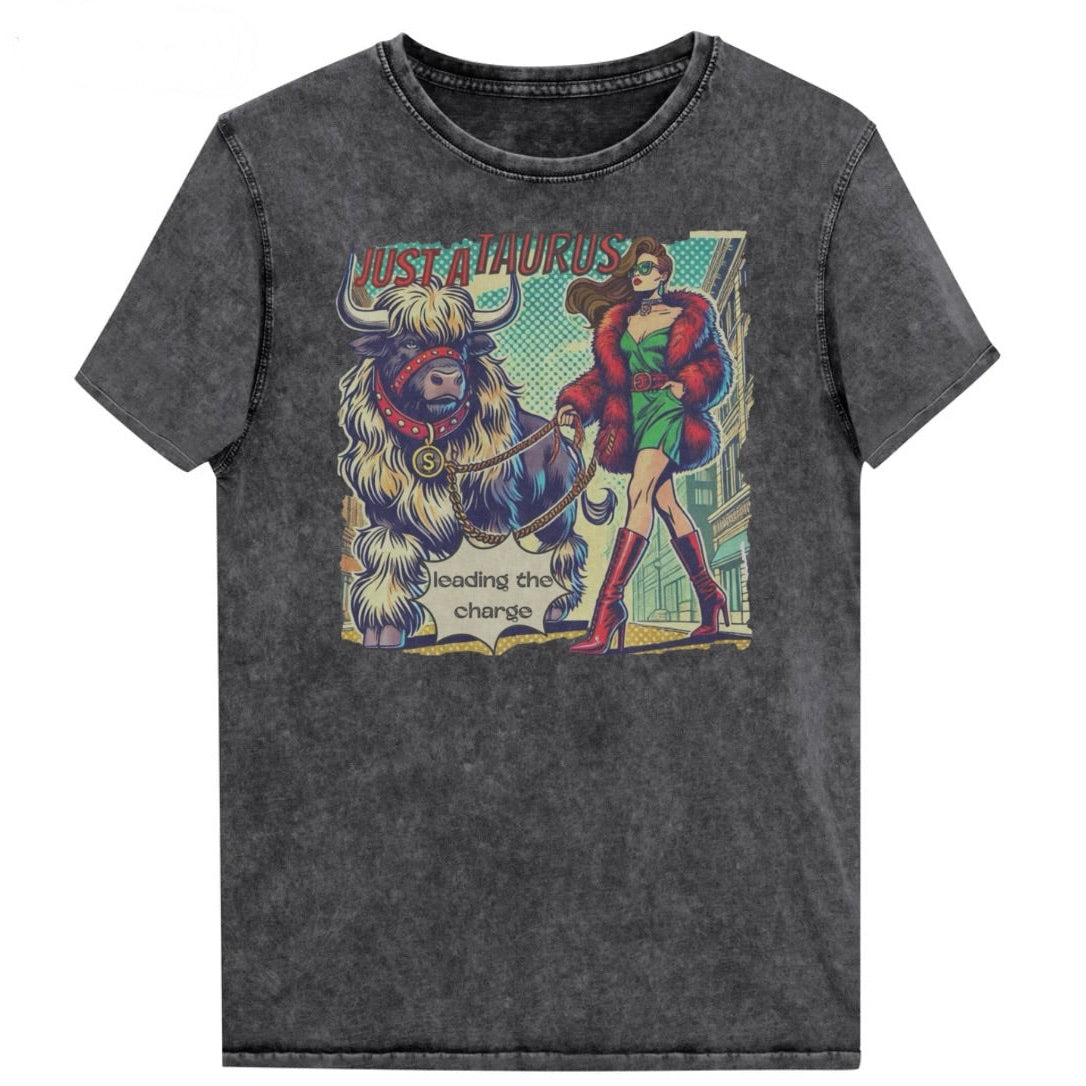 Flatlay of a unisex relaxed fit black vintage denim wash t-shirt with a retro pop-art taurus graphic featuring a brunette woman with long flowing straight hair, wearing a green dress with a red belt, red high-heeled boots and red fur coat, walking a furry bull with a red collar and medallion in city street captioned ‘Just a taurus leading the charge'. Branded RedBlonde in red on inside neck and right shoulder