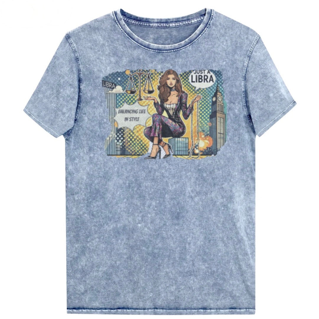 Flatlay of a unisex blue denim wash vintage t-shirt with a retro pop-art Brunette Libra graphic featuring a brunette woman, scales, and a city backdrop, captioned ‘Just a Libra, Balancing Life in Style’. Branded RedBlonde on inside neck and right sleeve