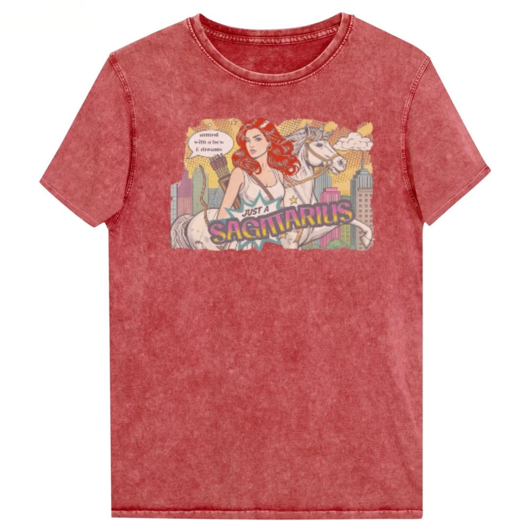 Flatlay of a unisex garnet red denim wash vintage t-shirt with a retro pop-art Redhead Sagittarius graphic featuring a blonde woman, with bow & arrows, white stallion, and a city backdrop, captioned ‘Just a Sagittarius, armed with a bow & dreams'. Branded RedBlonde on the inside neck and right sleeve