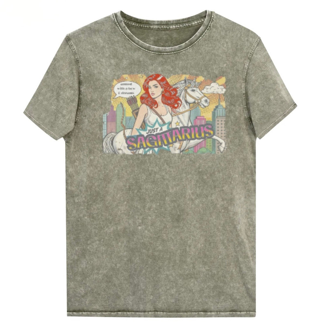 Flatlay of a unisex army green denim wash vintage t-shirt with a retro pop-art Redhead Sagittarius graphic featuring a blonde woman, with bow & arrows, white stallion, and a city backdrop, captioned ‘Just a Sagittarius, armed with a bow & dreams'. Branded RedBlonde on the inside neck and right sleeve