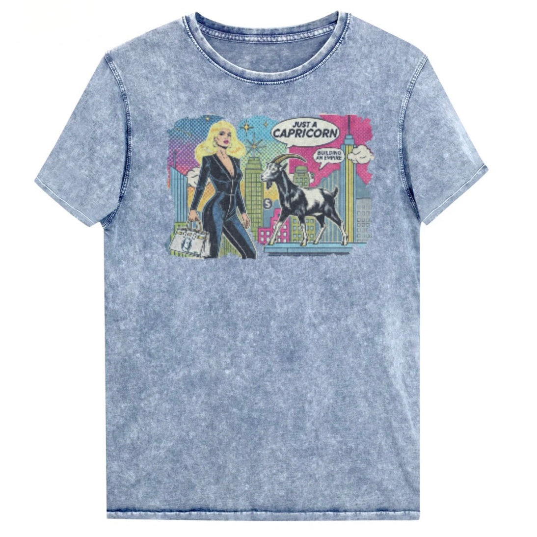 Flatlay of a unisex blue denim wash vintage t-shirt with a retro pop-art Capricorn graphic featuring a blonde haired woman in a black catsuit, carrying a bag, with a goat  and a city skyscraper backdrop, captioned ‘Just a Capricorn, Building an empire'. Branded RedBlonde in red on inside neck and right sleeve