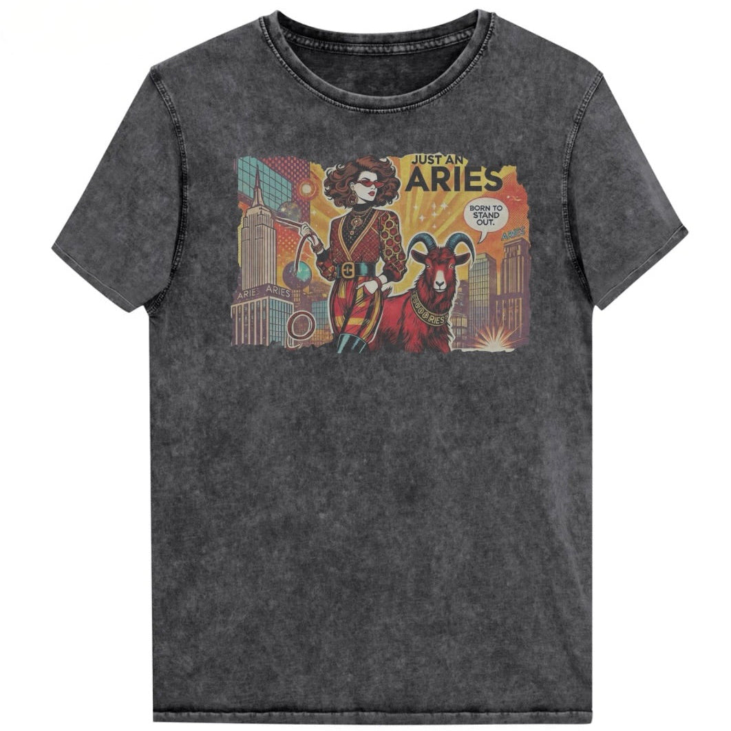 Flatlay of a unisex black denim wash vintage t-shirt with a retro pop-art brunette Aries graphic featuring a Brunette woman, wearing a belted catsuit and high boots with one hand in her pocket, with a ram by her side and a city backdrop, captioned ‘Just an Aries, born to stand out'. Branded RedBlonde in red on inside neck and right sleeve
