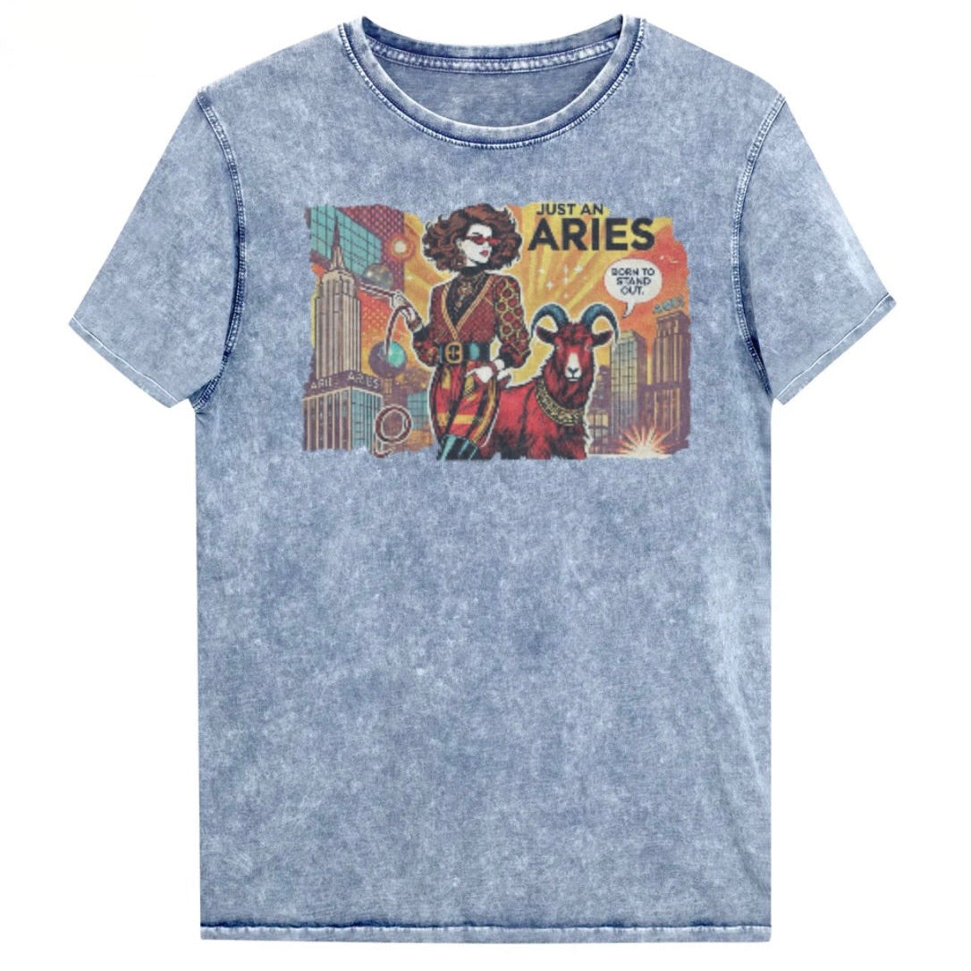 Flatlay of a unisex blue denim wash vintage t-shirt with a retro pop-art brunette Aries graphic featuring a Brunette woman, wearing a belted catsuit and high boots with one hand in her pocket, with a ram by her side and a city backdrop, captioned ‘Just an Aries, born to stand out'. Branded RedBlonde in red on inside neck and right sleeve