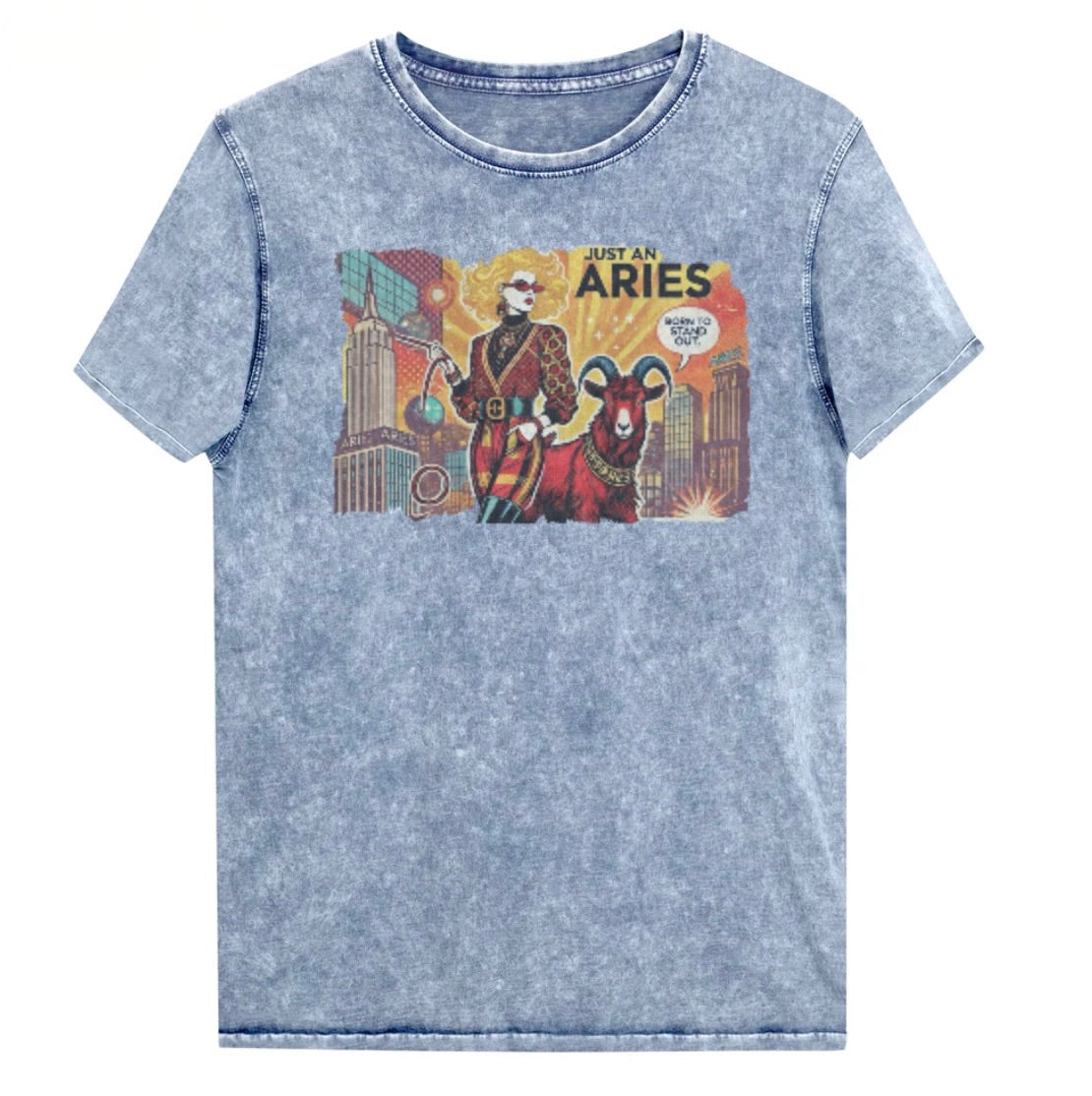 Flatlay of a unisex blue denim wash vintage t-shirt with a retro pop-art Aries graphic featuring a blonde woman, wearing a belted catsuit and high boots with one hand in her pocket, with a ram by her side and a city backdrop, captioned ‘Just an Aries, born to stand out'. Branded RedBlonde on inside neck and right sleeve
