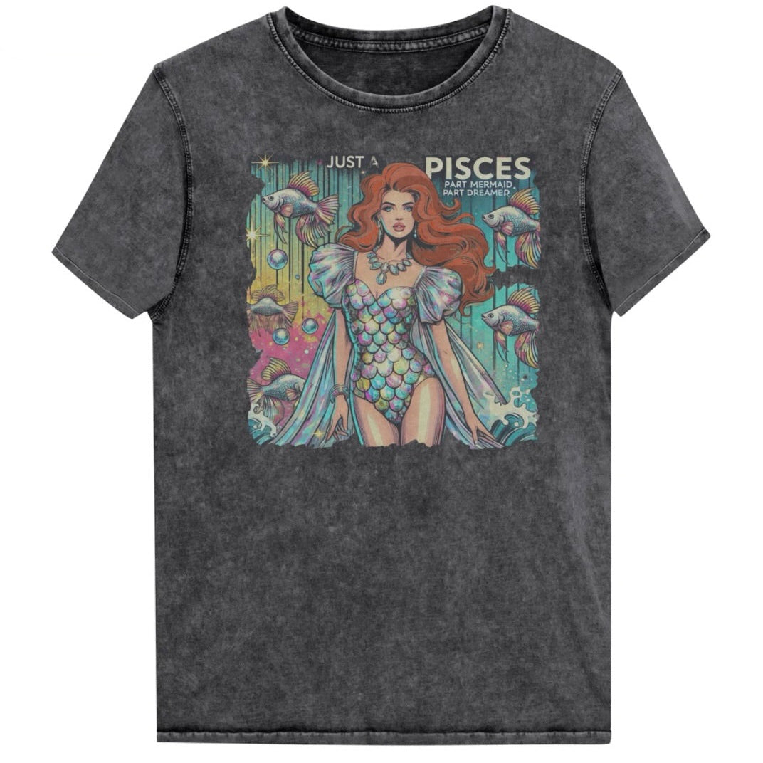 Flatlay of a unisex black denim wash vintage t-shirt with a retro pop-art Pisces graphic featuring a redhead woman in a fish-scale dress, with fishes and bubbles backdrop, captioned ‘Just a Pisces, Part Mermaid, Part Dreamer'. Branded RedBlonde in red on inside neck and right shoulder