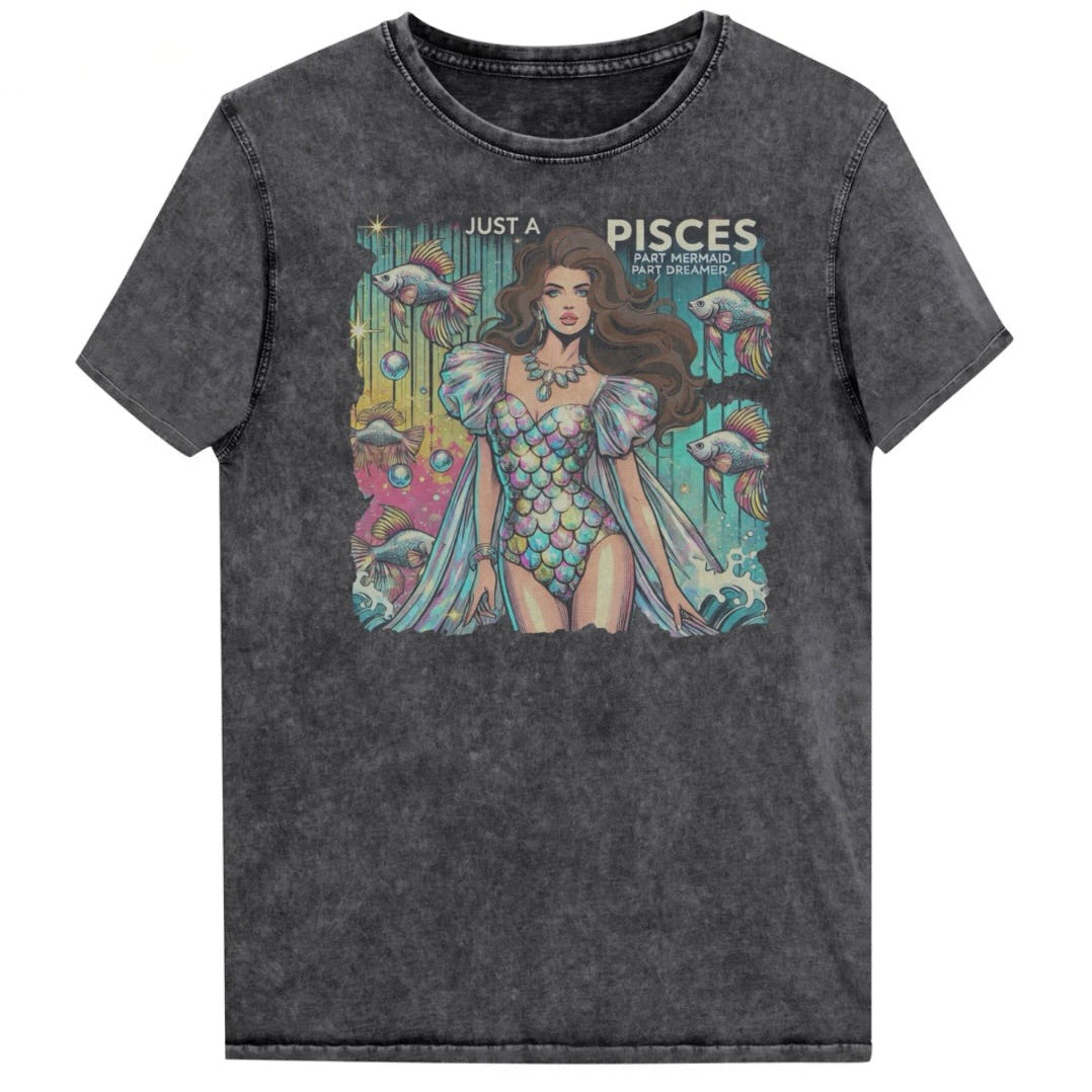 Flatlay of a unisex black denim wash vintage t-shirt with a retro pop-art Pisces graphic featuring a brunette woman in a fish-scale dress, with fishes and bubbles backdrop, captioned ‘Just a Pisces, Part Mermaid, Part Dreamer'. randed RedBlonde on inside neck and right shoulder