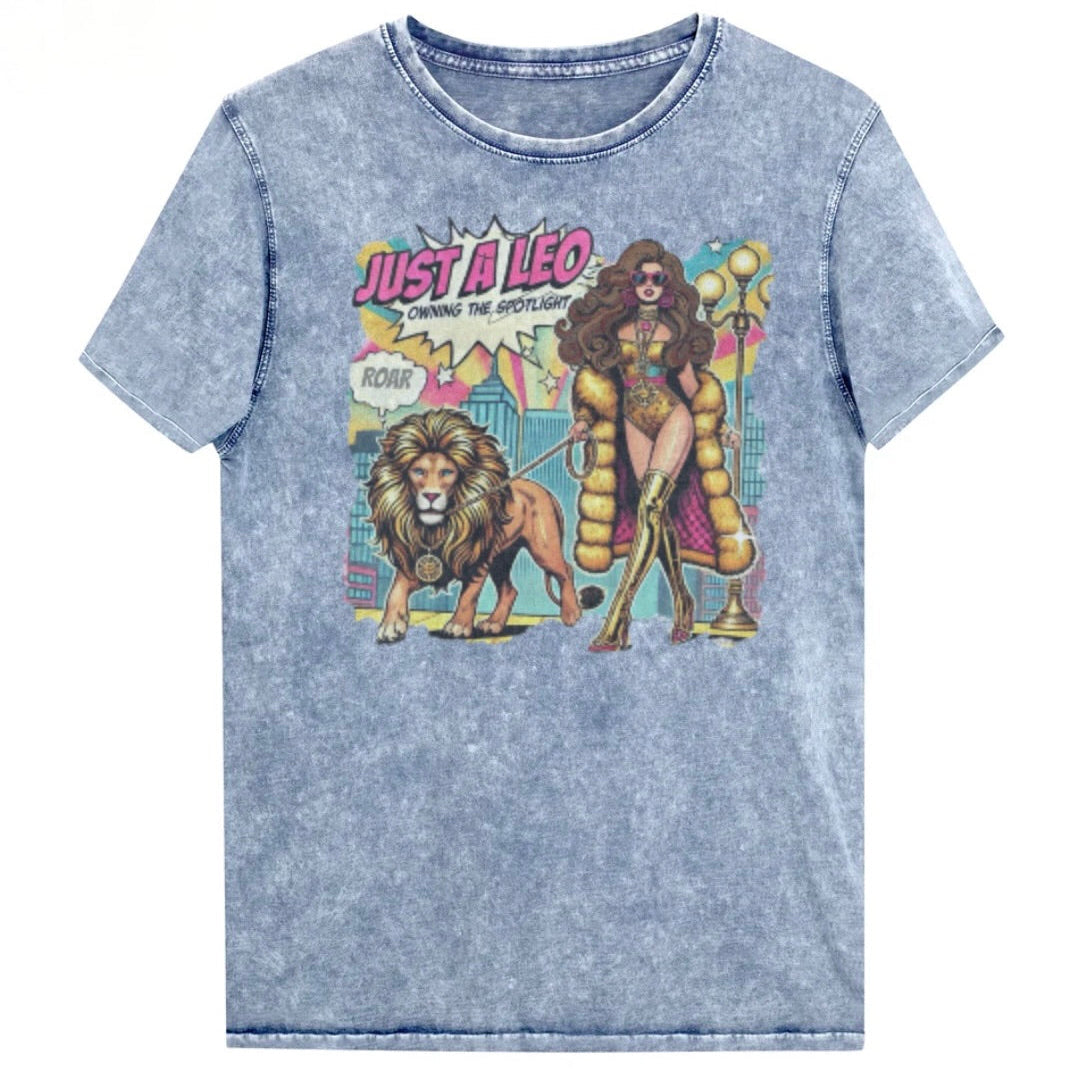 Flatlay of a unisex blue denim wash vintage t-shirt with a retro pop-art Brunette Leo graphic featuring a long haired brunette woman in a gold swimsuit, gold over the knee boots, gold medallion and long fur coat, walking a lion on a leash wearing a gold medallion, with a caption bubble 'Roar', with a city and round bulb street lights in the background captioned ‘Just a Leo, Owning the Spotlight'. Branded RedBlonde in red on inside neck and right shoulder