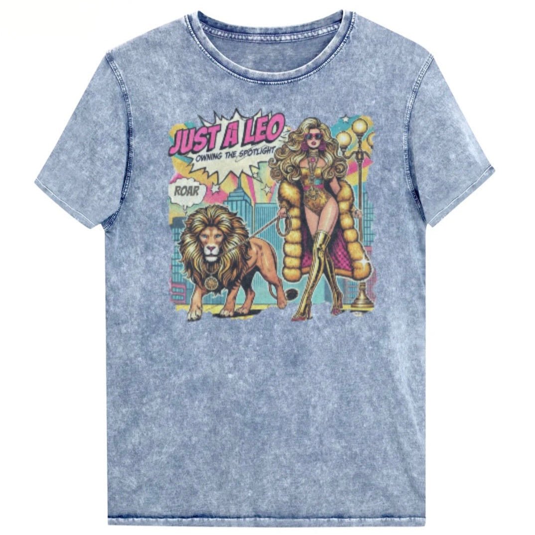 Flatlay of a unisex blue denim wash vintage t-shirt with a retro pop-art Leo graphic featuring a long curly haired blonde woman in a gold swimsuit, gold over the knee boots, gold medallion and long fur coat, walking a lion on a leash wearing a gold medallion, with a caption bubble 'Roar', with a city and round bulb street lights in the background captioned ‘Just a Leo, Owning the Spotlight'. Branded RedBlonde on inside neck and right shoulder