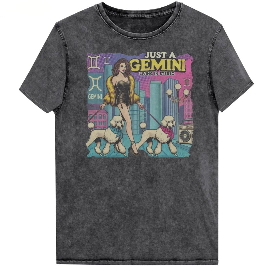 Flatlay of a unisex black denim wash vintage t-shirt with a retro pop-art Gemini graphic featuring a brunette woman, in a short catsuit and fur coat walking two poodle dogs with neck scarfs with a city backdrop and a gettoblaster ‘Just a Gemini, Living in Stereo'. Branded RedBlonde in red on inside neck and right shoulder