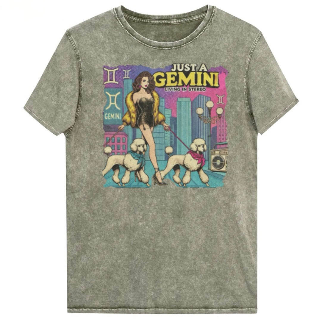 Flatlay of a unisex army green denim wash vintage t-shirt with a retro pop-art Gemini graphic featuring a brunette woman, in a short catsuit and fur coat walking two poodle dogs with neck scarfs with a city backdrop and a gettoblaster ‘Just a Gemini, Living in Stereo'. Branded RedBlonde in red on inside neck and right shoulder