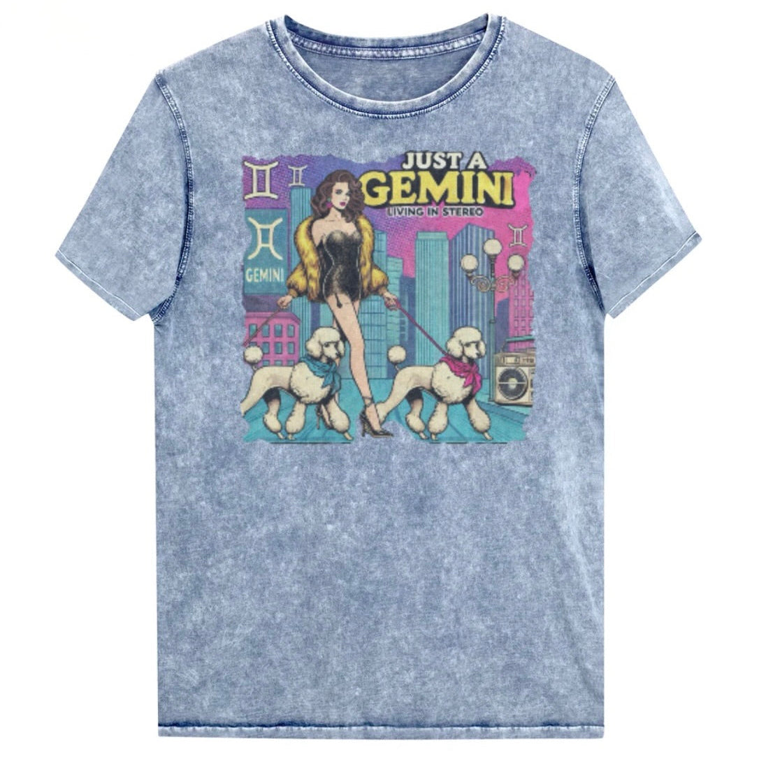 Flatlay of a unisex blue denim wash vintage t-shirt with a retro pop-art Gemini graphic featuring a brunette woman, in a short catsuit and fur coat walking two poodle dogs with neck scarfs with a city backdrop and a gettoblaster ‘Just a Gemini, Living in Stereo'. Branded RedBlonde in red on inside neck and right shoulder