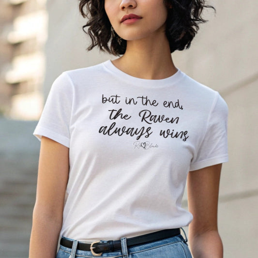 Jet black haired woman wears a white unisex t-shirt featuring the handwritten-style slogan “but in the end, the Raven always wins” in Hillbear font  in light gray text across the chest, signed off RedBlonde. Branded “RedBlonde London on inside the collar and on the right sleeve
