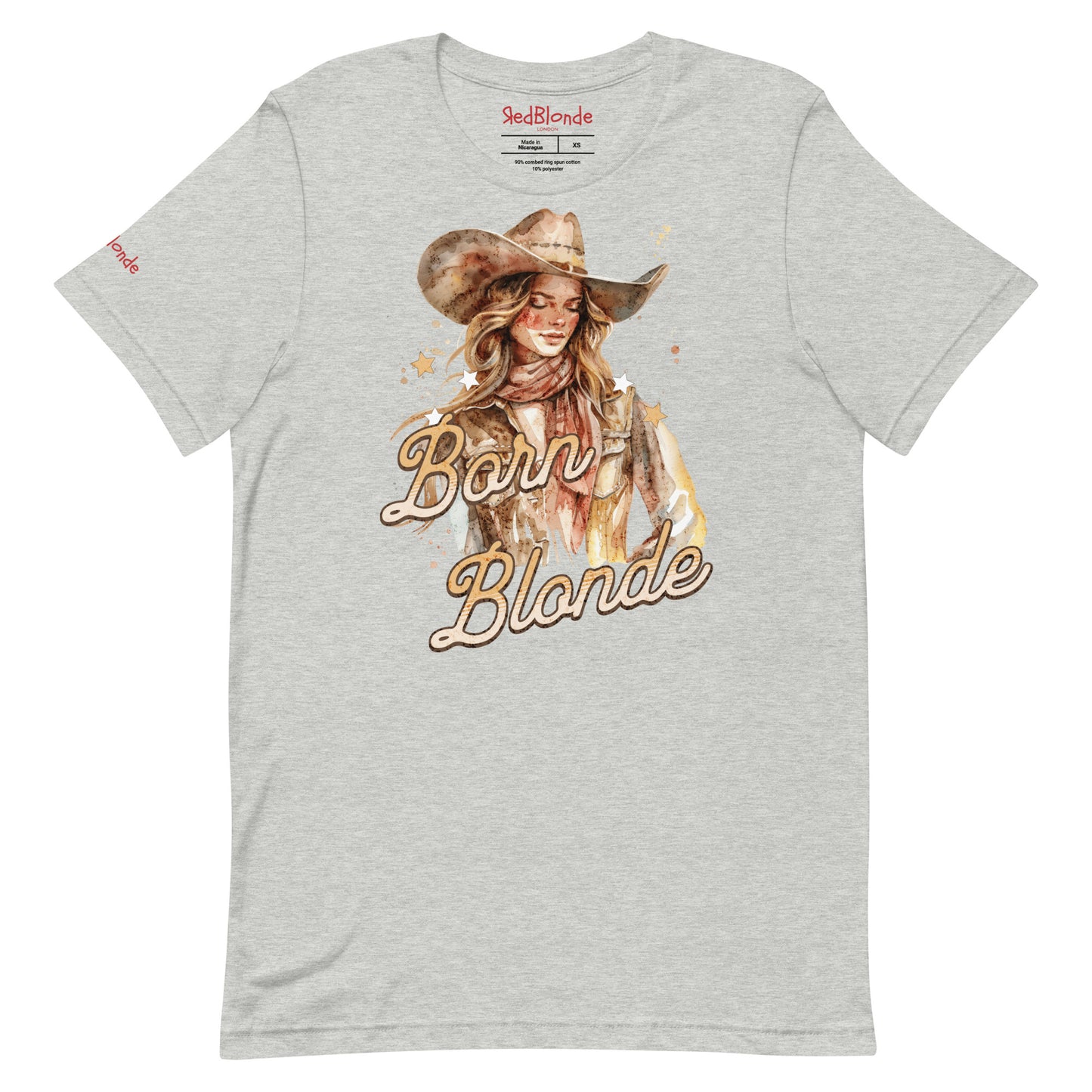 Light heather grey unisex t-shirt featuring a watercolor-style illustration of a blonde cowgirl wearing a wide-brimmed hat and scarf. The graphic includes the slogan “Born Blonde” in a bold, vintage-style adventurer font. RedBlonde branding appears on the inner neck label and right sleeve.