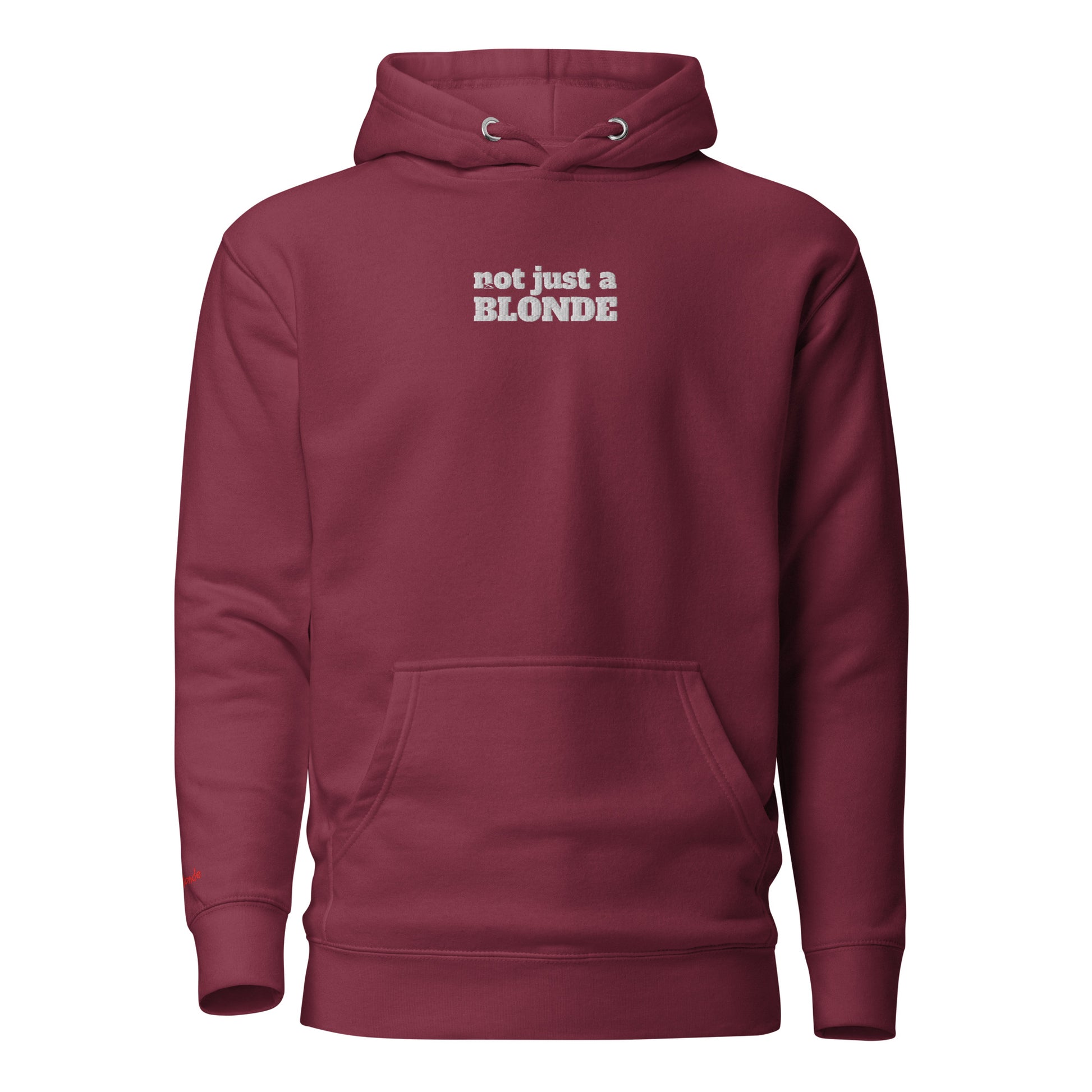 Front view of a maroon unisex hoodie featuring white embroidered text that reads “not just a BLONDE” across the chest. The hoodie has a drawstring hood and a front kangaroo pocket, giving it a bold yet casual streetwear look. It is branded Redblonde on the inside neck and right sleeve