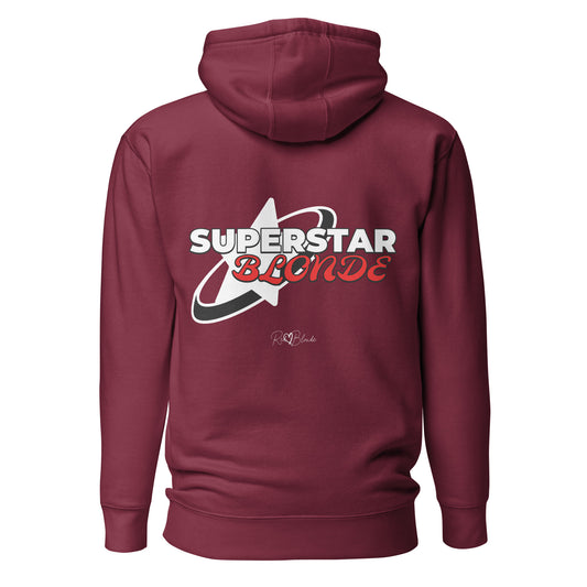A maroon unisex pullover hoodie with a large back graphic design. The print features a bold white star with a swoosh around it and the words “SUPERSTAR BLONDE” in white and red retro-style Monsierrat and Molle lettering. The design also includes a small signature logo “R & B Blonde” underneath. Branded RedBlonde on inside neck and right sleeve