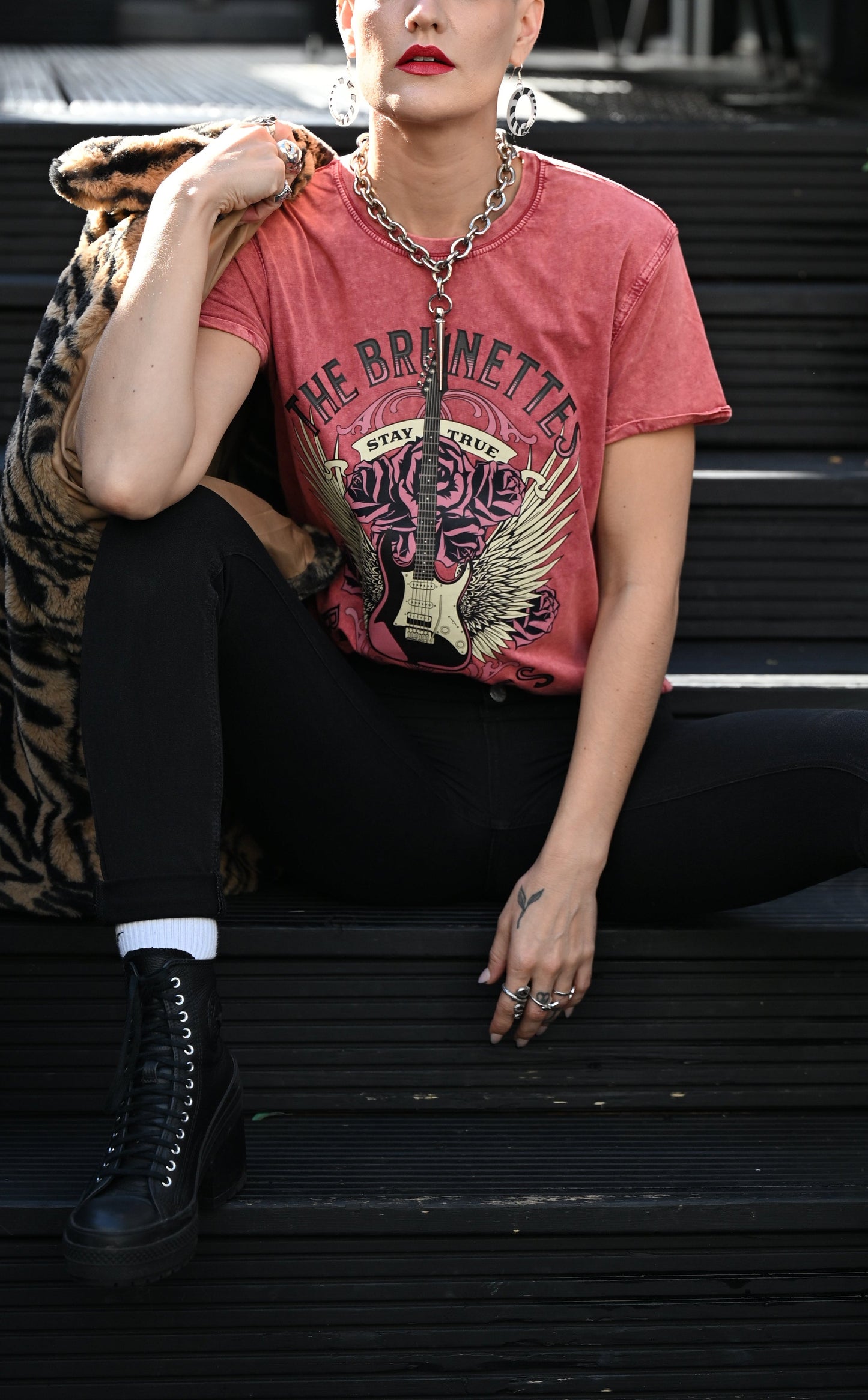 Model wears a red garnet denim wash unisex t-shirt with a burnt pink & beige graphic of a guitar with bird wings emerging from the side. The graphic features ‘THE BRUNETTES’. in Brookfield font above the guitar, ‘STAY TRUE' across the top and 'BREAK RULES’ underneath. Branded RedBlonde London in inside neck and right sleeve.