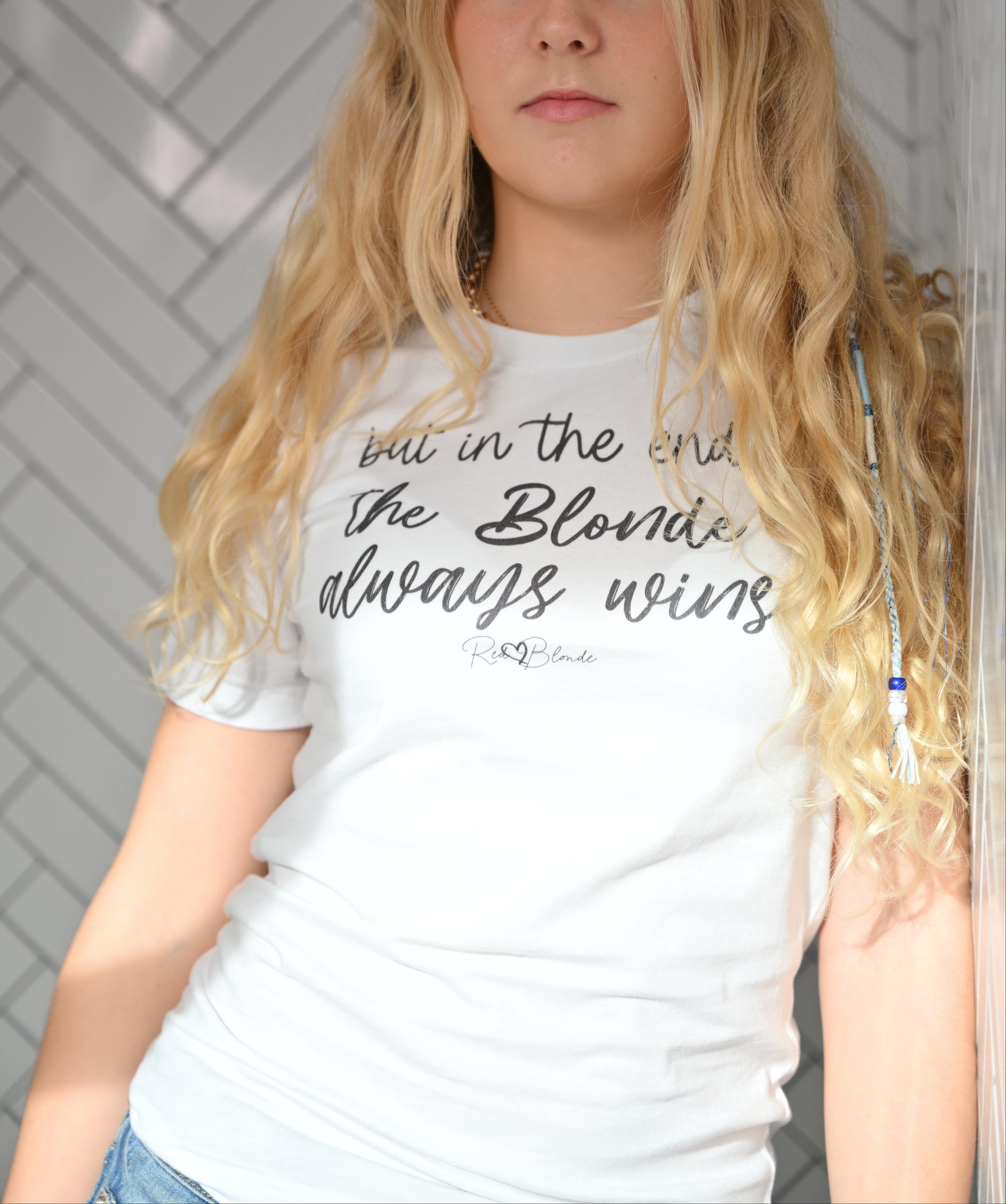Blonde woman wears white unisex t-shirt featuring the handwritten-style slogan “but in the end, the Blonde always wins” in Hillbear font  in light gray text across the chest, signed off RedBlonde. Branded “RedBlonde London on inside the collar and on the right sleeve