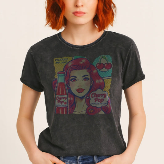 Redhead wears a unisex vintage black denim wash t-shirt with a pop-art graphic of a redheaded woman with a bottle of cherry pop, cherry graphic and the words 'Cherry Pop, delicious and light' in talk bubble. Branded RedBlonde on inside neck and right sleeve in red 