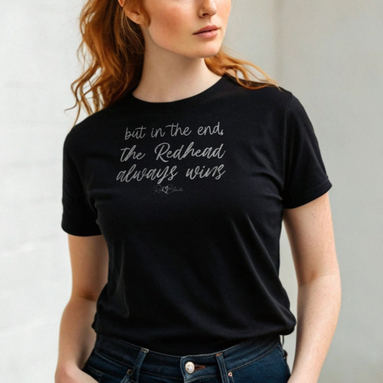 Redhead woman wears a black unisex t-shirt featuring the handwritten-style slogan “but in the end, the Redhead always wins” in Hillbear font  in dark gray text across the chest, signed off RedBlonde. Branded “RedBlonde London on inside the collar and on the right sleeve