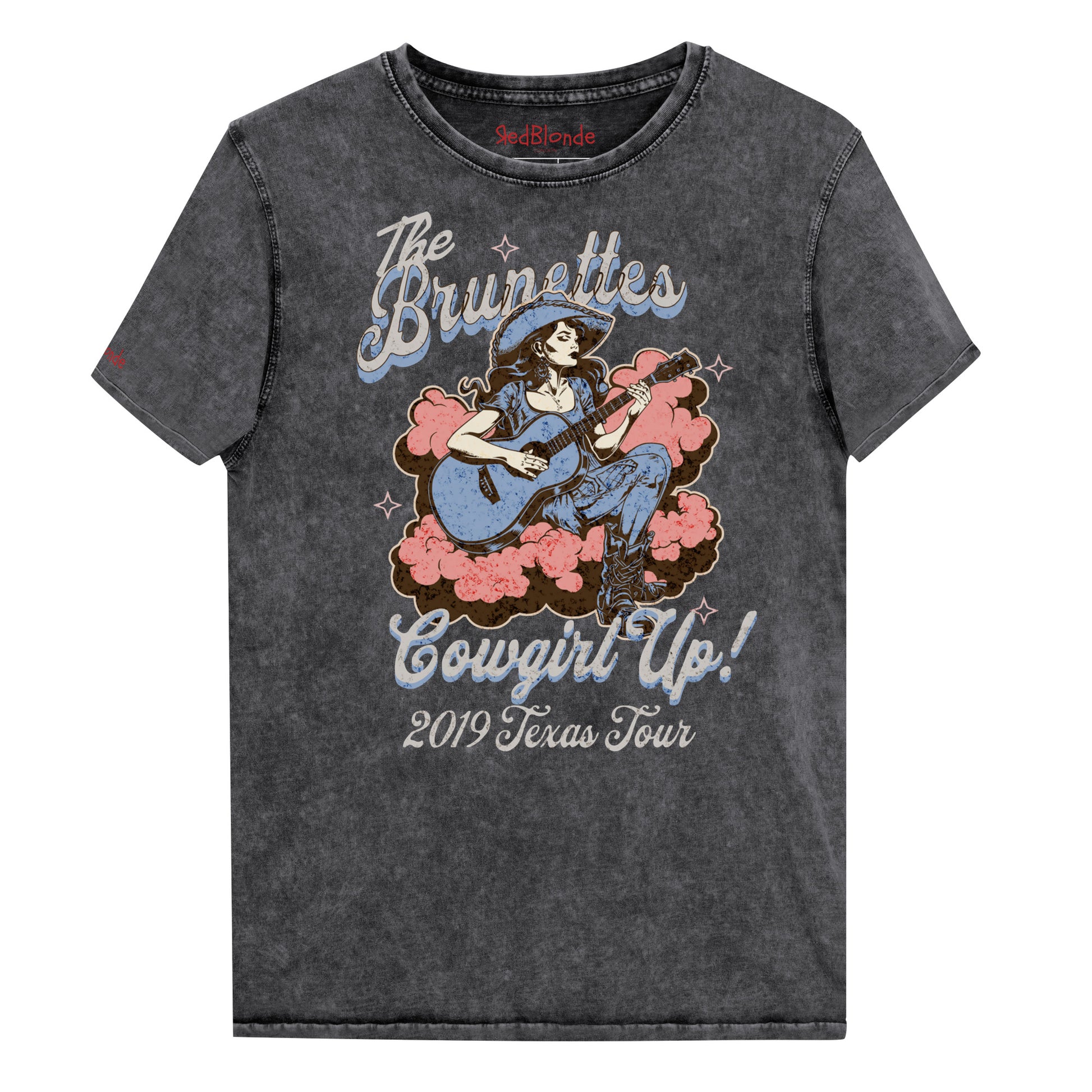 Vintage black unisex t-shirt with a faded wash, featuring a retro graphic of a cowgirl playing a guitar surrounded by pink clouds. Text reads 'The Brunettes – Cowgirl Up! 2019 Texas Tour' in a Western-style font. Branded RedBlonde London on the inside neck and right sleeve