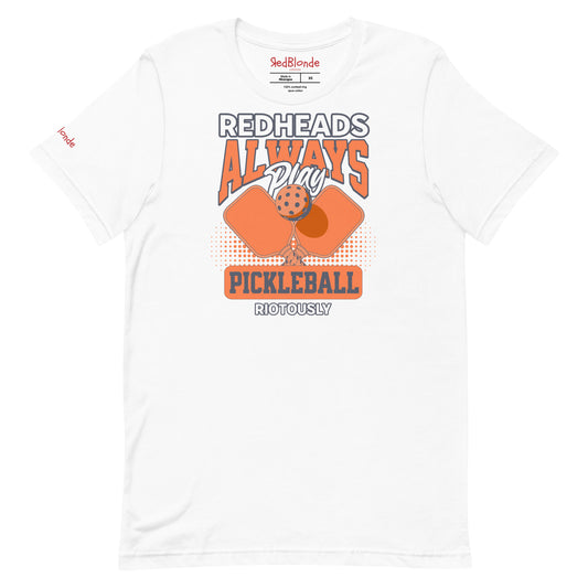 White unisex t-shirt with orange graphic that reads "Redheads Always Play Pickleball Riotously," featuring pickleball paddles and ball. Branded RedBlonde on inside neck and right sleeve