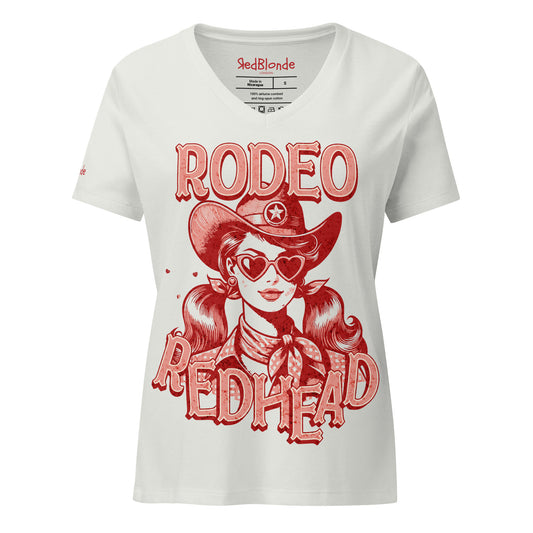 Women's silver V-neck t-shirt featuring a bold red vintage illustration of a cowgirl with heart-shaped sunglasses and pigtails, wearing a wide-brimmed cowboy hat and scarf. Text reads "RODEO REDHEAD" in large Western-style lettering. Branded RedBlonde on inside neck and right sleeve.