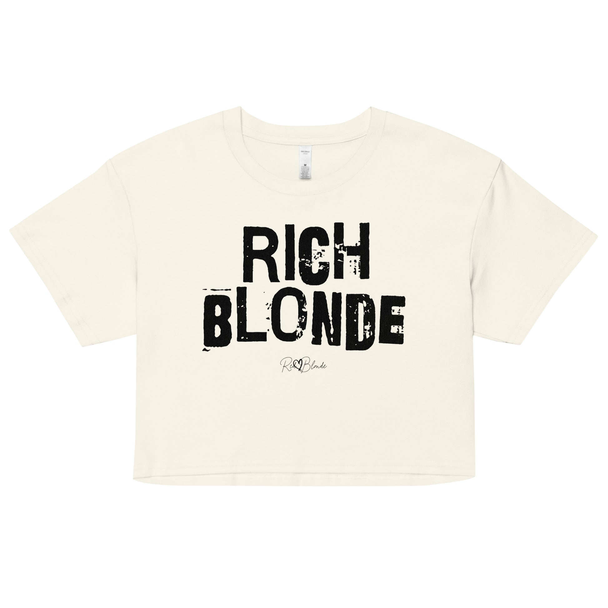 a natural coloured crop top with a relaxed fit, short sleeves, and a wide crew neckline. The front features bold black distressed lettering reading “RICH BLONDE” with the RedBlonde signature logo underneath in white.