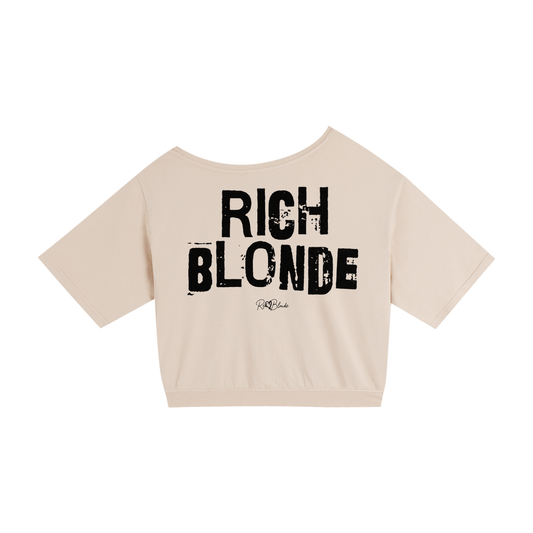 apricot asymmetrical shoulder t-shirt with bold black Ed Gein font “RICH BLONDE" slogan on the front and RedBlonde logo beneath.