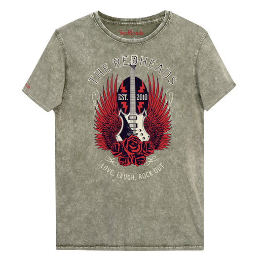 A flatlay of a army green denim wash unisex t-shirt with a graphic of a black & white guitar with red bird wings emerging from the side. The graphic features ‘THE REDHEADS' in Brookfield font in a semicircle above the guitar, while ‘Love, laugh, rock out’ is underneath. Branded RedBlonde London in inside neck and right sleeve