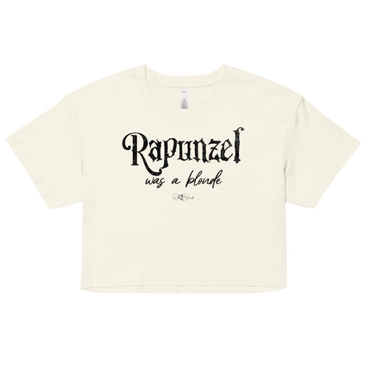 Natural-colored women’s crop top featuring black fairytale spiky text that reads “Rapunzel" and the phrase “was a blonde” written underneath in an elegant cursive script. signed off with the RedBlonde heart signature logo