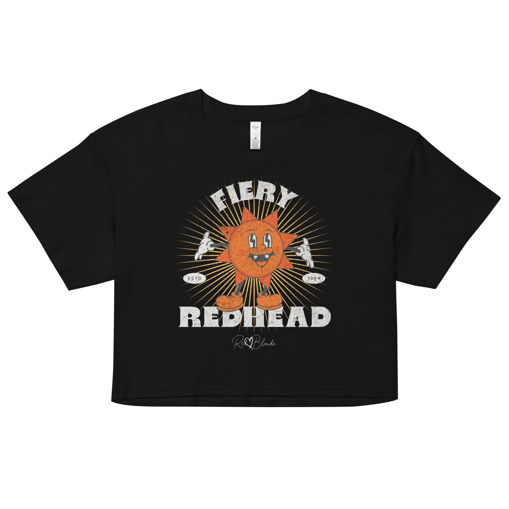 Black women’s crop top with a bold retro graphic of a smiling orange cartoon sun character, surrounded by radiant sunbeams. The text reads ‘Fiery Redhead’ in distressed white Belzebuth lettering with small details including ‘ESTD 1994’ and the RedBlonde signature logo beneath."