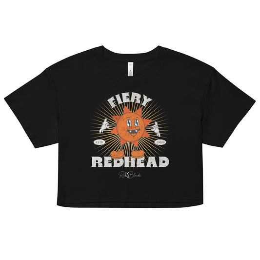 Black women’s crop top with a bold retro graphic of a smiling orange cartoon sun character, surrounded by radiant sunbeams. The text reads ‘Fiery Redhead’ in distressed white Belzebuth lettering with small details including ‘ESTD 1994’ and the RedBlonde signature logo beneath."